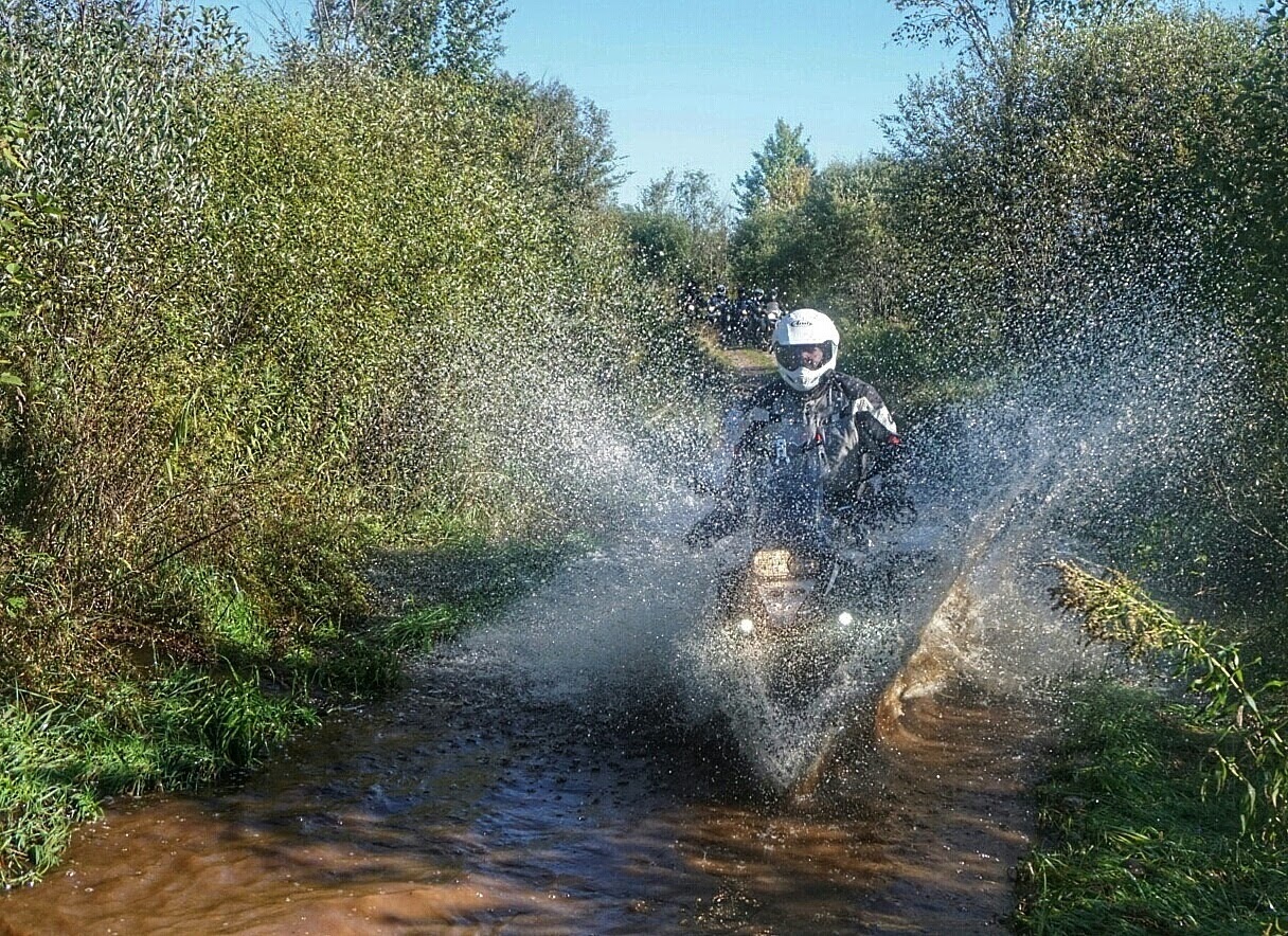 Motorcyclist riding through a shallow stream on an adventure trail, symbolizing exploration, challenge, and personal growth.