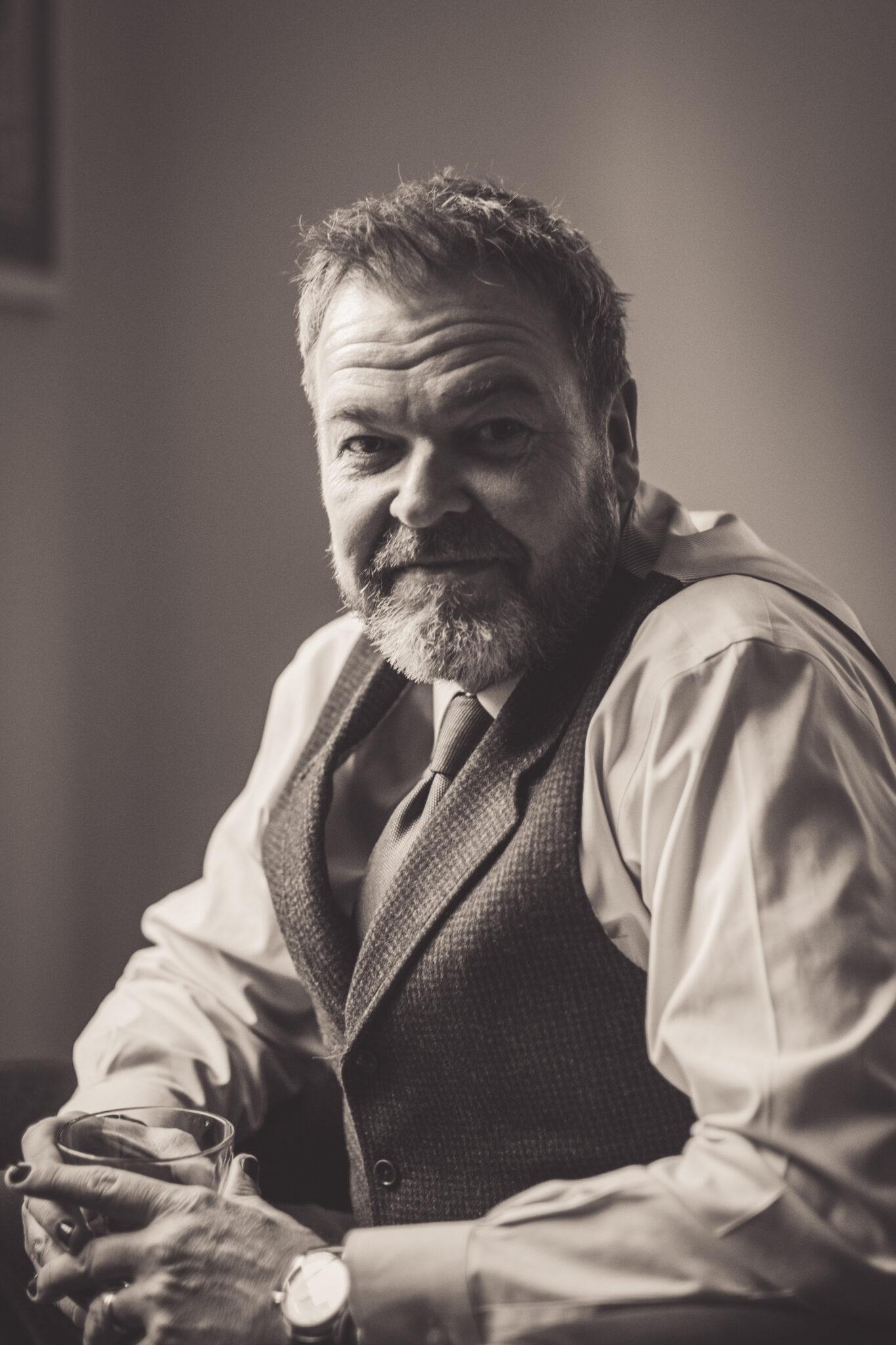 Kevin Ladd, author of Go BIG Or Go FCK Yourself*, sitting indoors in a vest and tie, smiling during a black-and-white portrait session.