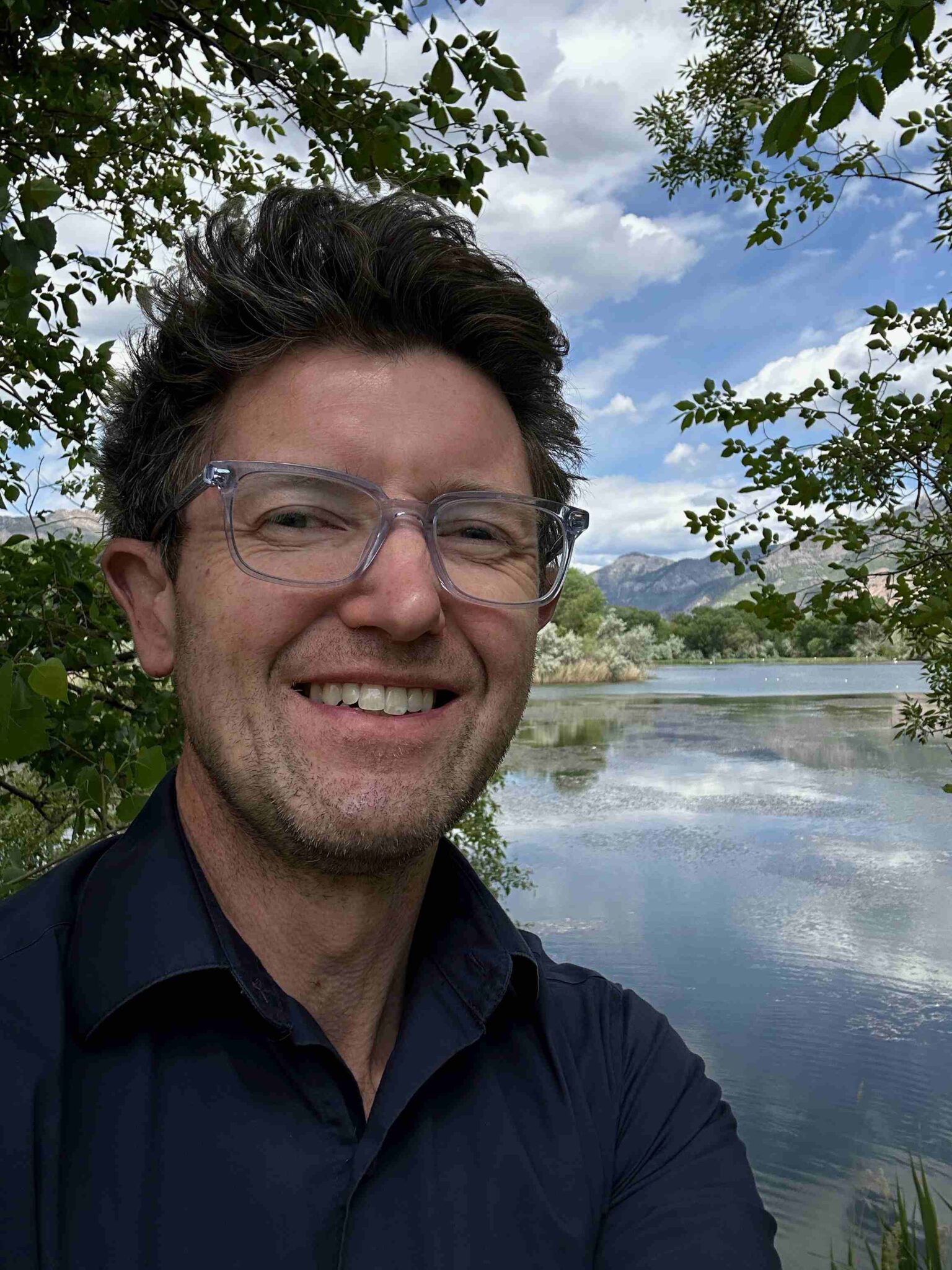 Chris Bentley smiling outdoors beside a lake and mountains
